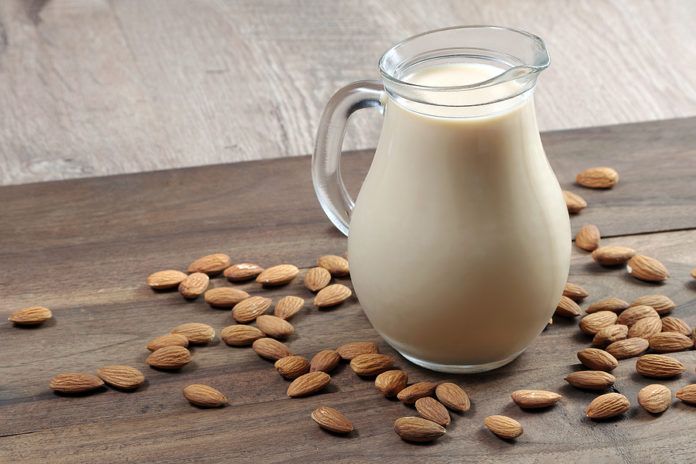 Almond milk in a glass jug on a wooden table. almonds and milk